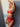Frau trägt roter BH, Suspender, String von Venereea. Sie lehnt sich an einer weissen Wand ab und legt einen Arm über ihren Kopf