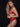 Blonde Frau steht vor einer schwarzem Hintergrund und trägt rote, sexy Venereea Unterwäsche.  BH - Strapsenhalter - String